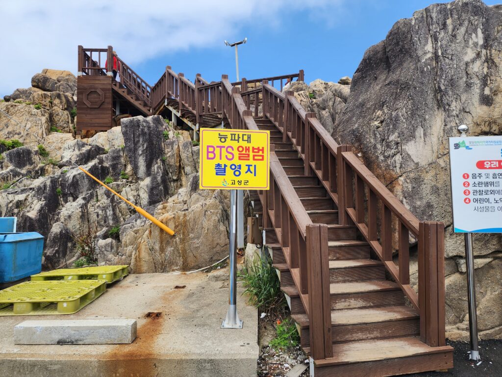 The wooden staircase entrance to Neungpadae Geopark with a yellow sign marking the BTS winter package filming location.