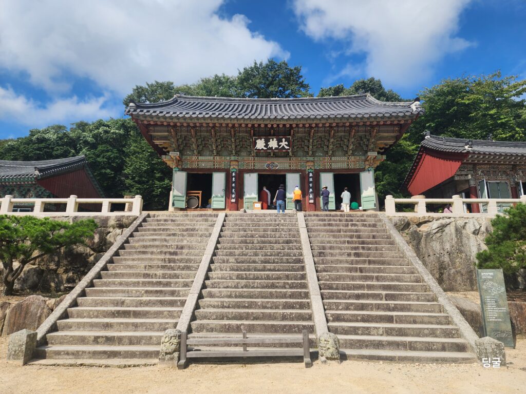 Grand stone staircase leading to the main prayer hall at Beomeosa Temple under fluffy white clouds.