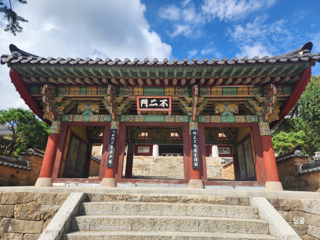 The ornate traditional Dancheong painted wooden gate at Beomeosa Temple in Busan with stone steps under a bright blue sky.