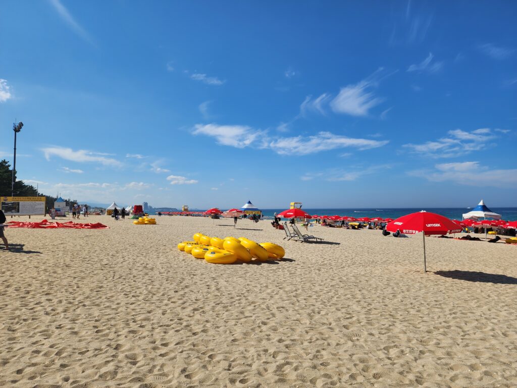 Bright blue sky over Gyeongpo Beach with yellow inflatable tubes arranged on the white sand.