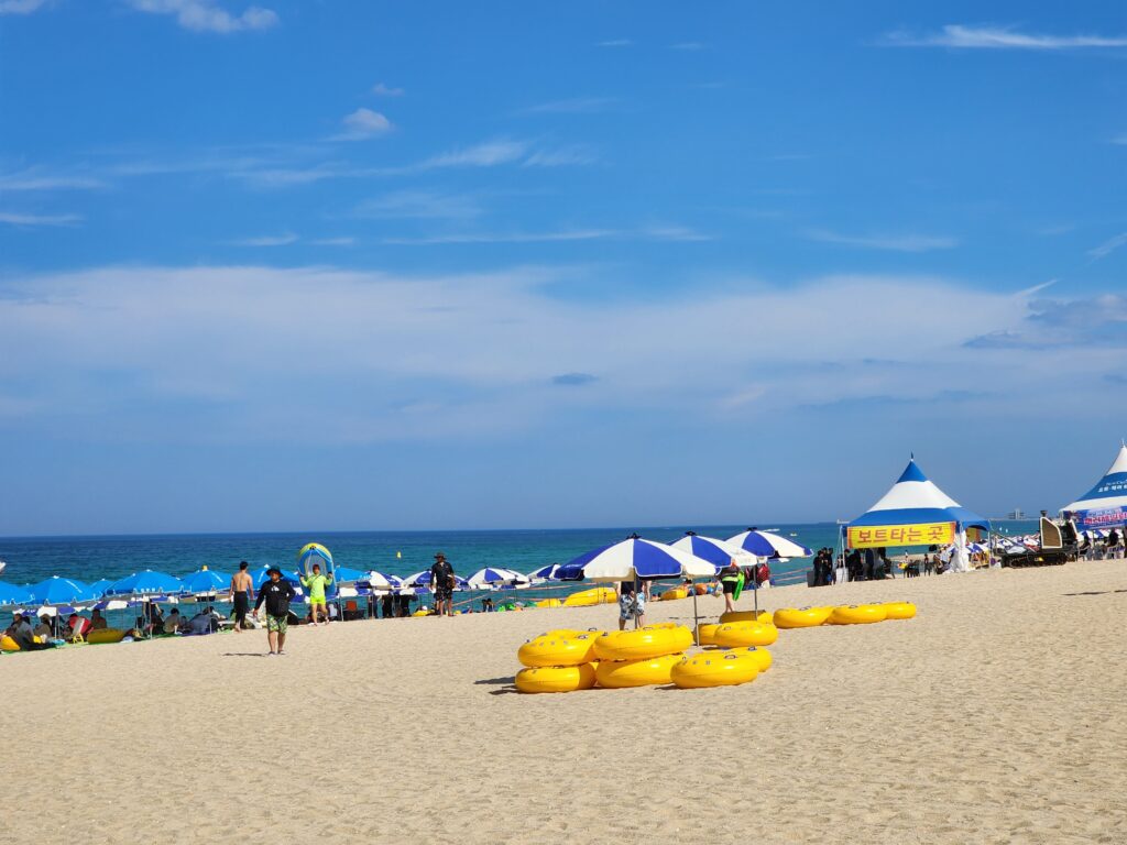 Sunny day at Gyeongpo Beach featuring stacked yellow tubes and beach umbrellas along the shoreline.