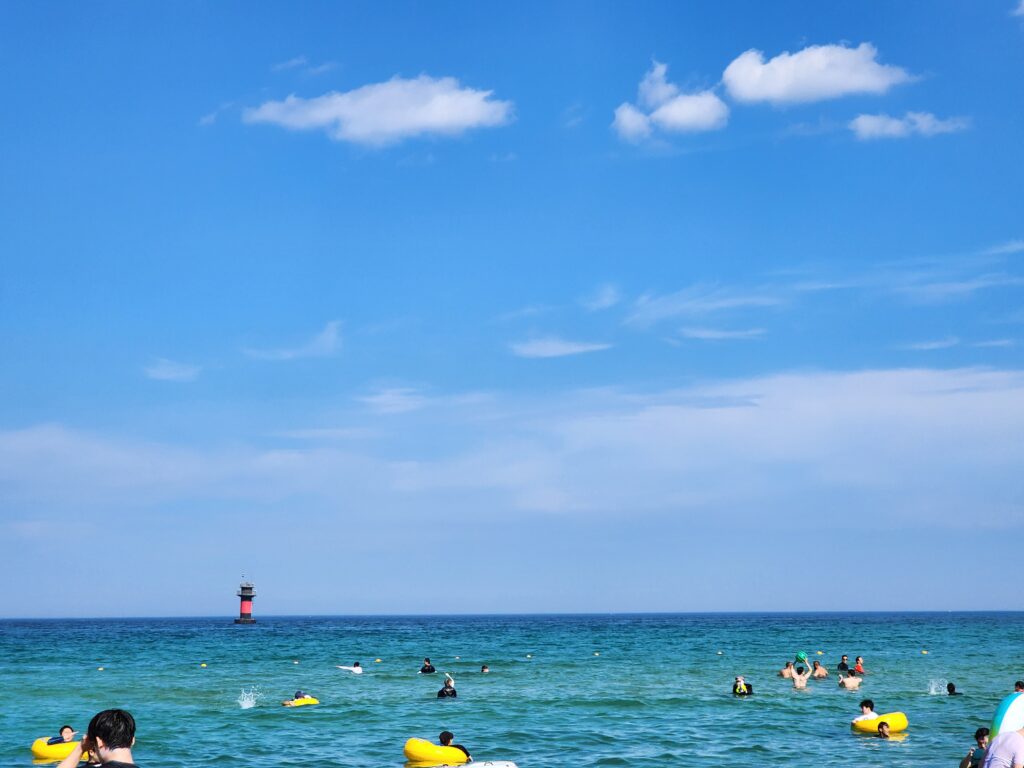 Beachgoers enjoying the clear ocean water at Gyeongpo Beach on a sunny day.