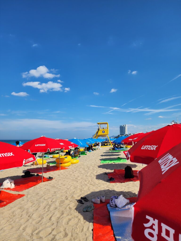 Rows of red beach umbrellas and a yellow lifeguard tower on a wide sandy beach.