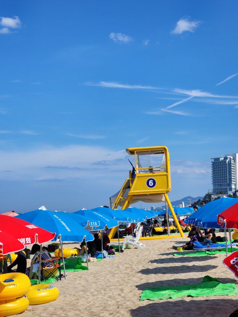 Yellow lifeguard tower standing on Gyeongpo Beach surrounded by blue and red sun umbrellas.