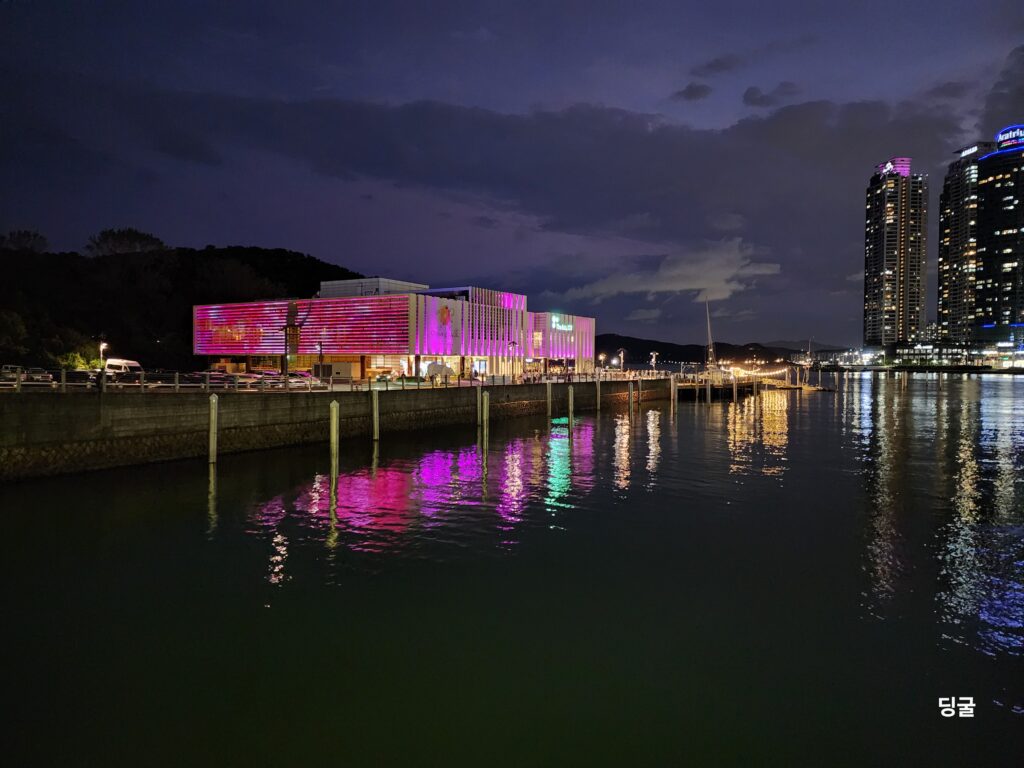 Illuminated modern waterfront building with warm lights reflected on the water at night.