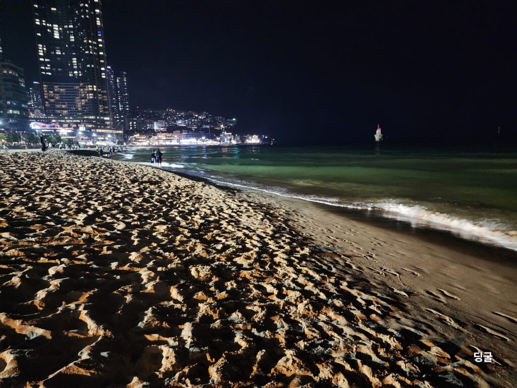 Gentle ocean waves hitting the sandy shoreline of Haeundae Beach at night.