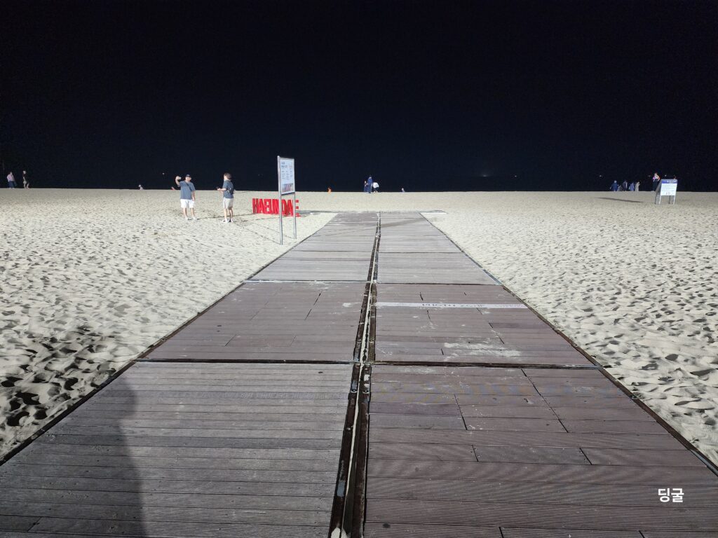 Wooden boardwalk path leading across the dark sandy beach of Haeundae at night.